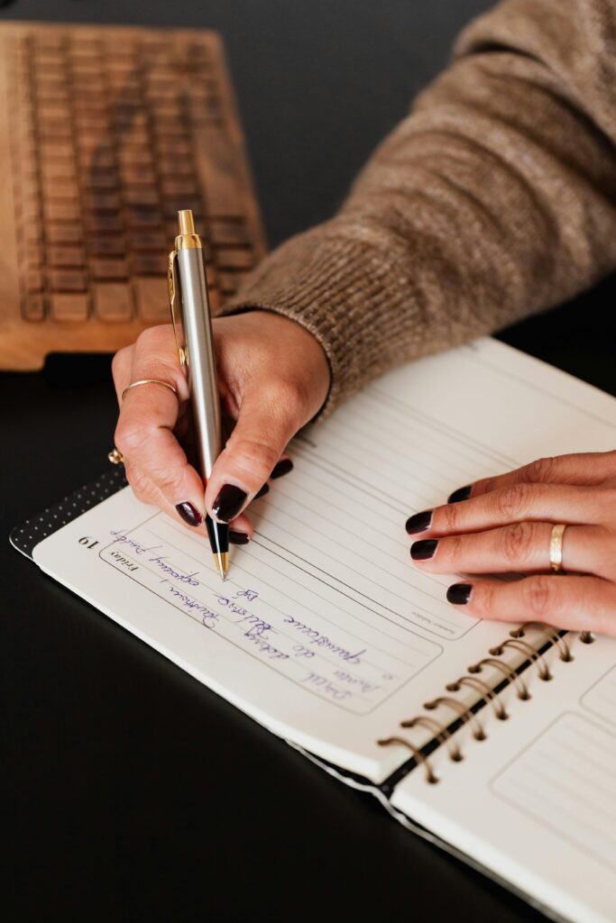 Close-up of a woman's hands writing in a planner on a desk. Perfect for productivity and organization themes.